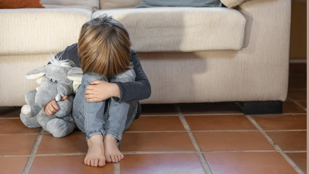 Petit garçon assis au sol, serrant son jouet en peluche, illustrant les conséquences psychologiques de la garde alternée