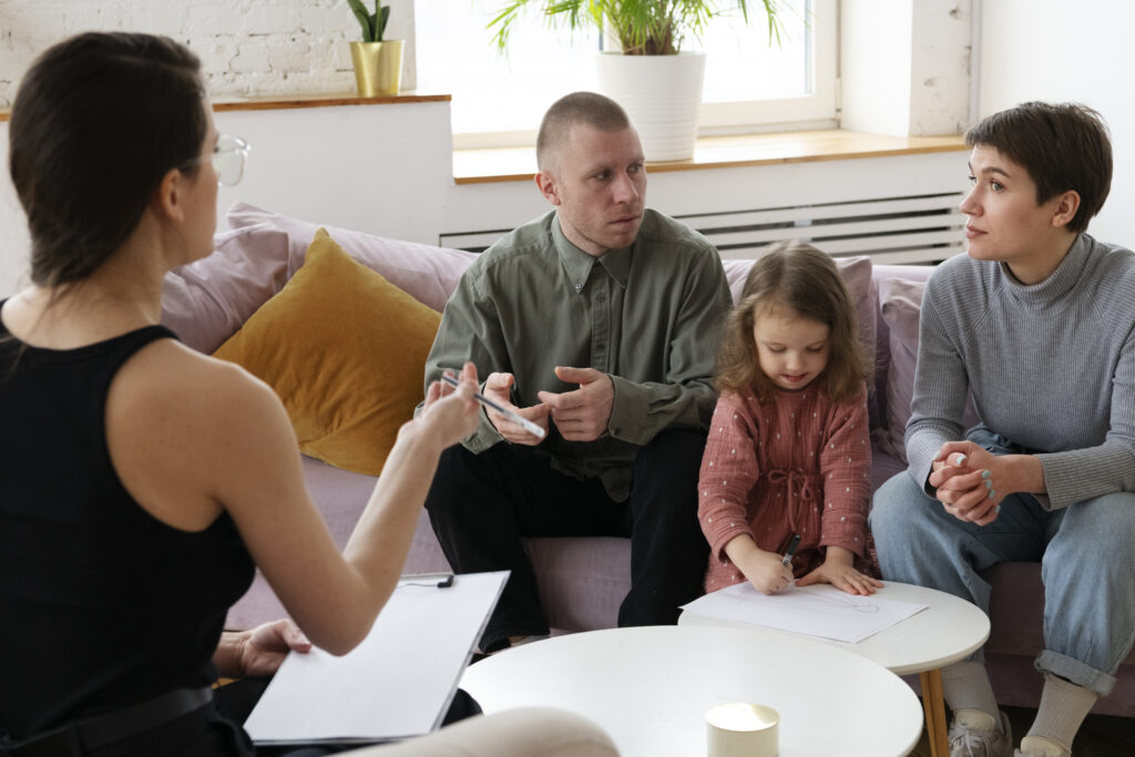 Parents séparés accompagnés par une thérapeute familiale pendant que leur enfant dessine