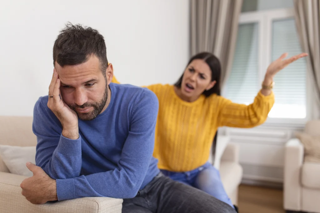 Crise de couple illustrée par une femme en colère face à son partenaire abattu dans le salon
