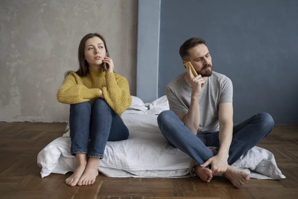Problème de couple, homme et femme assis dos à dos sur un lit, parlant au téléphone avec un air préoccupé.