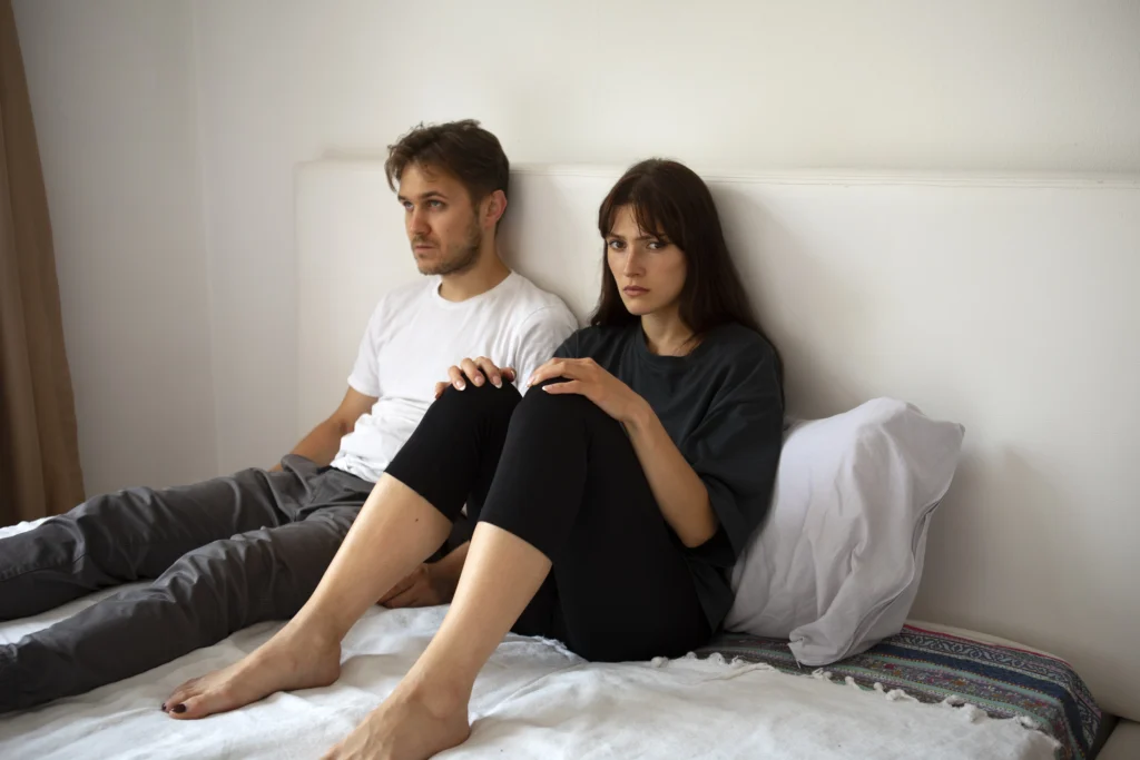 Couple en crise assis sur un lit, illustrant une séparation de couple et un manque de communication