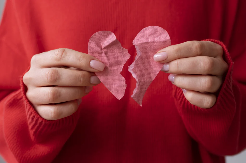 Mains tenant un cœur en papier déchiré, symbole de rupture en amour